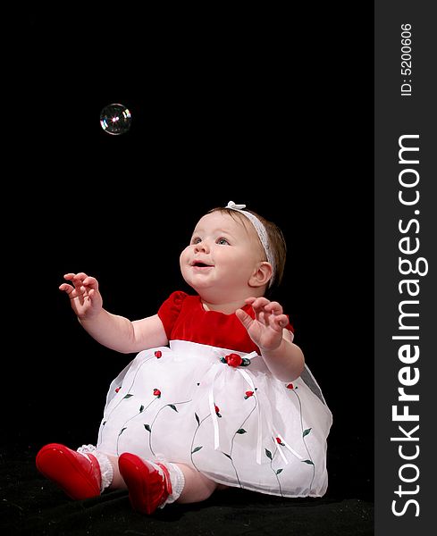 Little girl in red and white dress looking up in awe at a single bubble. Little girl in red and white dress looking up in awe at a single bubble.