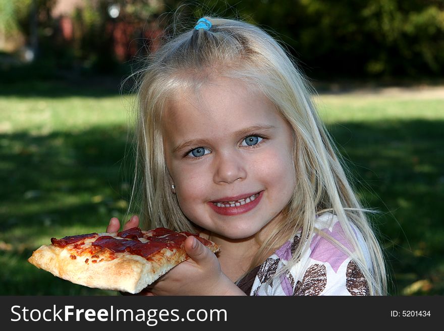 Sweet little girl eating pizza slice and smiling