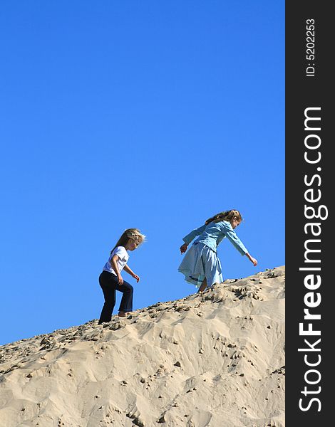 Two beautiful white caucasian girl children playing on a sand dune on the beach. Two beautiful white caucasian girl children playing on a sand dune on the beach