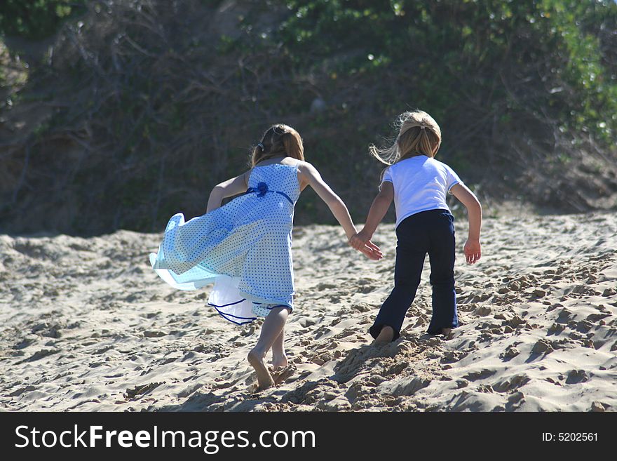 Two white caucasian girl sisters on the beach playing on a sand dune holding hands