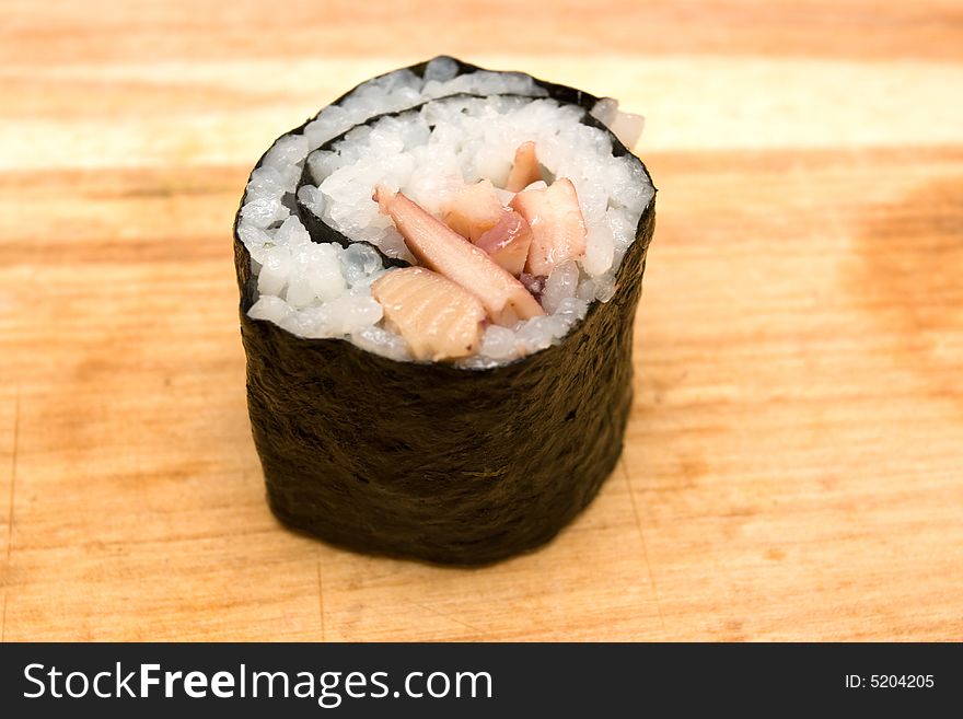 Closeup of sushi roll with squid on cutting board.