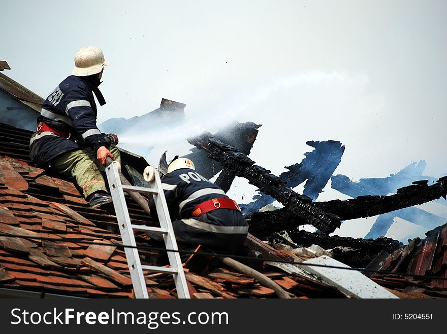 Two firemans in action on the roof of a burning house