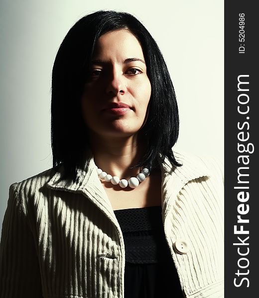 A high-key portrait about a happy attractive lady with black hair who is looking ahead and she has a charming look. She is wearing a white coat, a black dress, and a white necklace. A high-key portrait about a happy attractive lady with black hair who is looking ahead and she has a charming look. She is wearing a white coat, a black dress, and a white necklace.