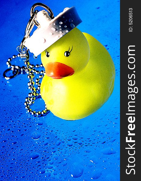 A colourful image of a rubber duck with a bath plug on his head that makes him look like a sailor ducky. the background is blue and is covered with little droplets
