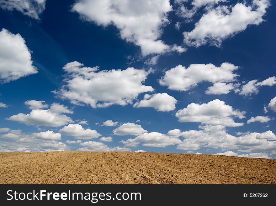 Blue sky with clouds over ploughed field.