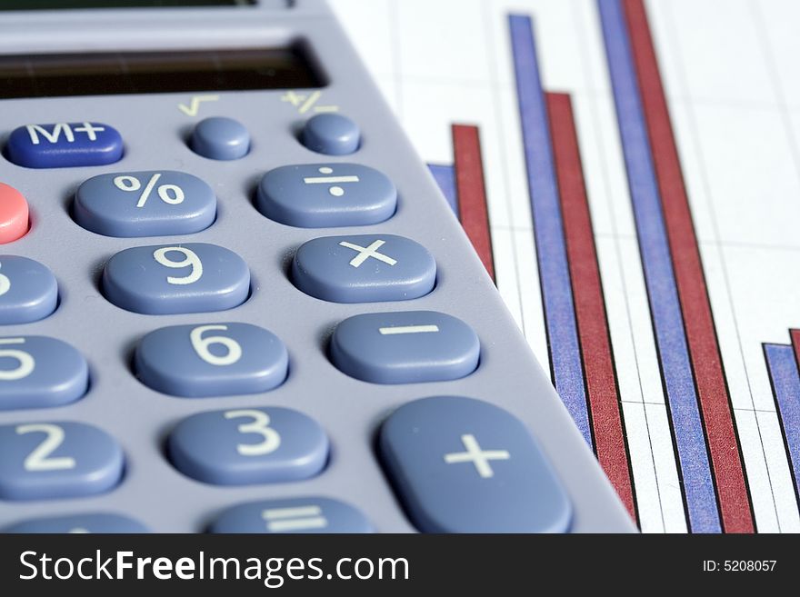 Close up of a blue calculator next to a red and blue bar chart on a white background. Close up of a blue calculator next to a red and blue bar chart on a white background