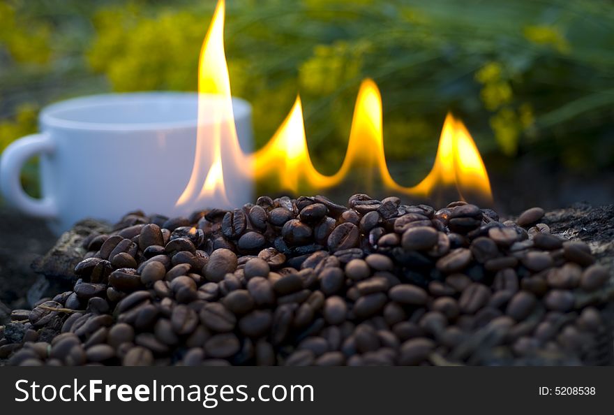 Burning, roasted coffee beans with a cup of coffee in background