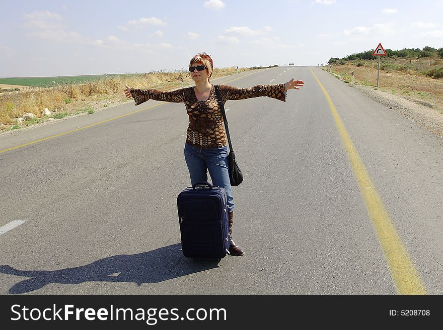 A young female hitch-hiker with her luggage. A young female hitch-hiker with her luggage