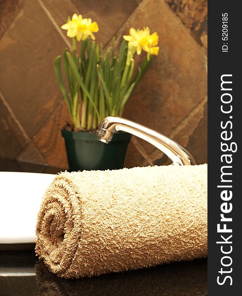 Beige rolled up towel next to a white ceramic basin with daffodil flowers in the bathroom. Beige rolled up towel next to a white ceramic basin with daffodil flowers in the bathroom