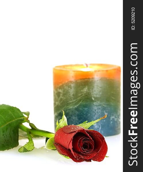 Single red rose with droplets and burning candle over white background