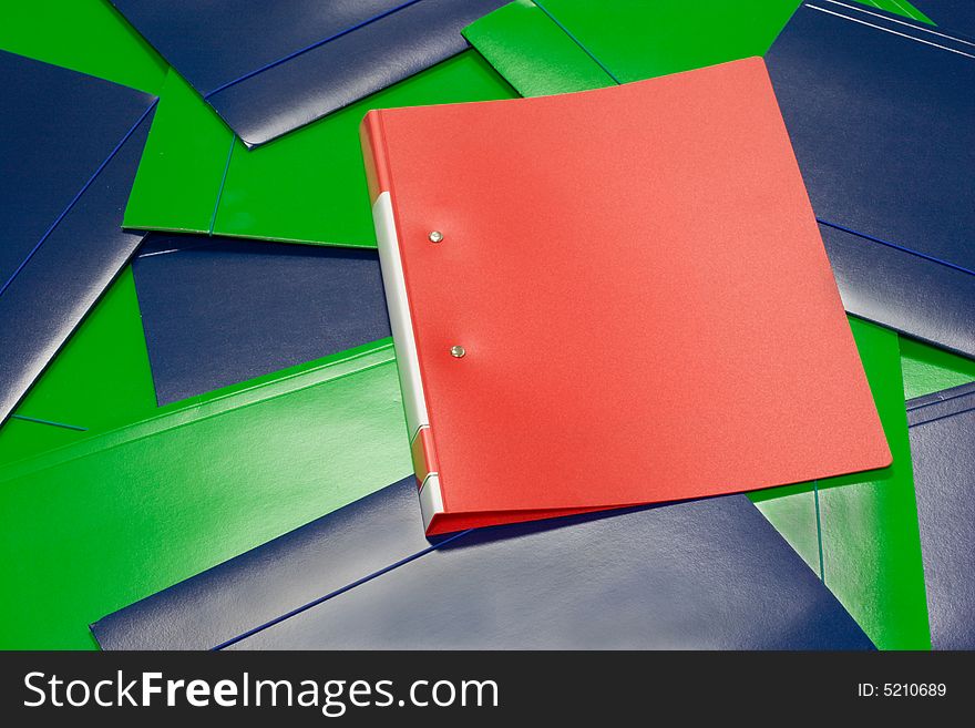 A single red folder, lying on a heap of green and blue folders