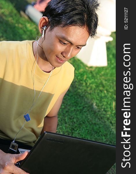 Young man with laptop and music on green grass. Young man with laptop and music on green grass