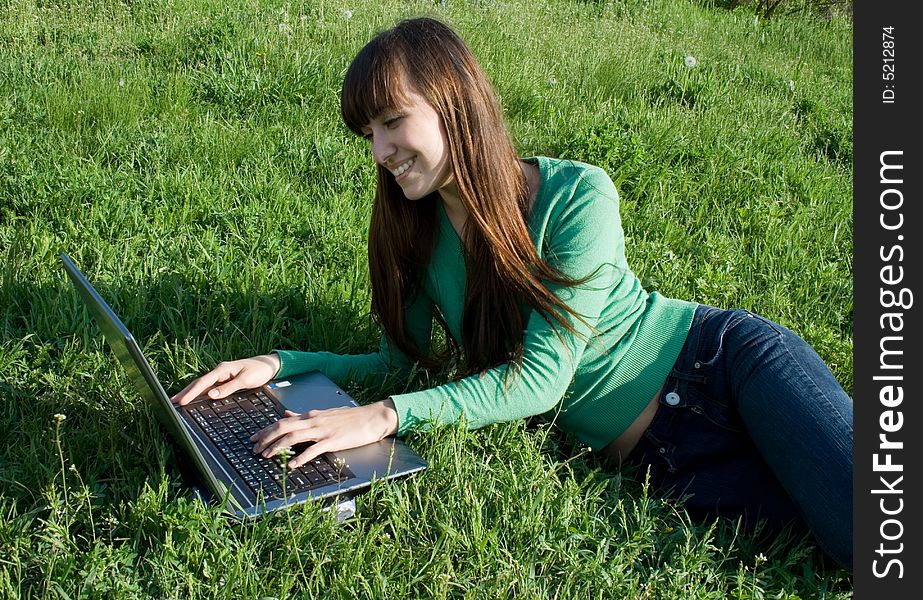 Happy young girl with laptop on meadow