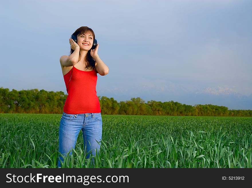 Pretty young woman with headphones in a wheat field enjoying music