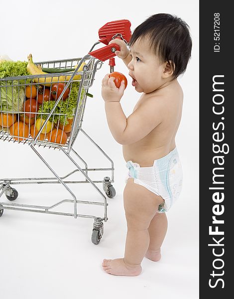 Baby pushes a shopping cart with fruit and vegetables