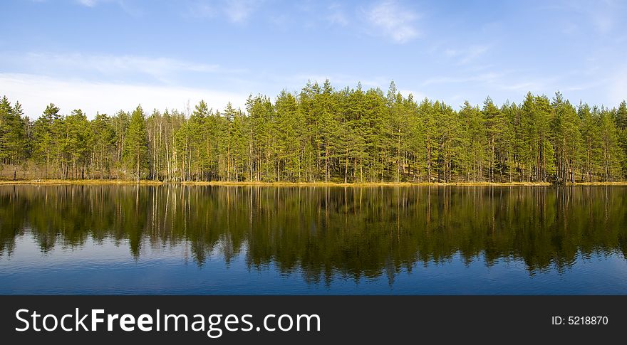 White  clouds, blue sky and green forest on far bank of the lake.