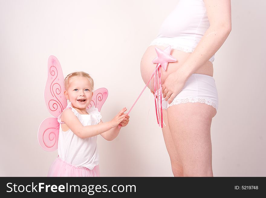 A little fairy points her magic wand at her mothers pregnant belly. A little fairy points her magic wand at her mothers pregnant belly