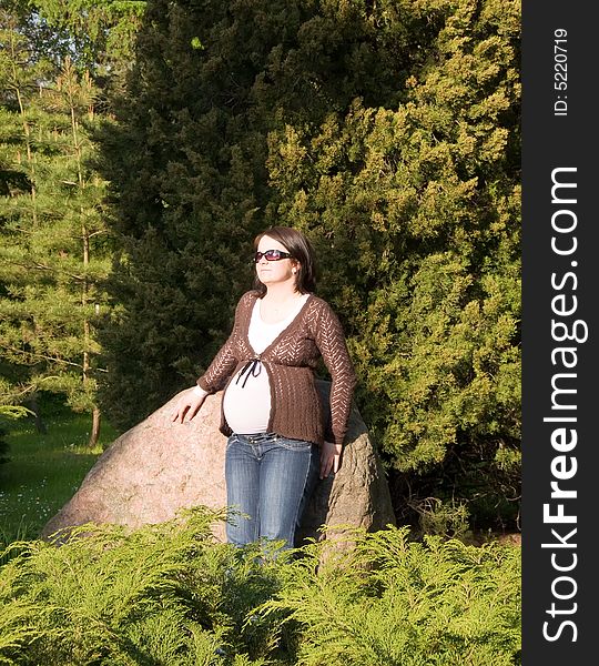 Pregnant woman taking sunbath while leaning against stone in the park. Pregnant woman taking sunbath while leaning against stone in the park