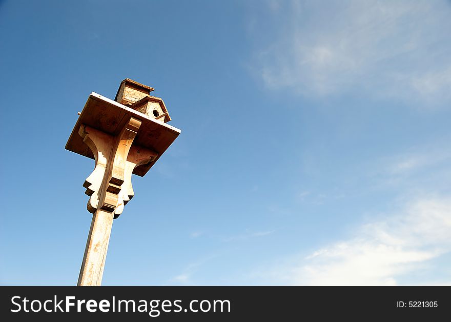 A wooden birdhouse on top of a pole with clouds in the background