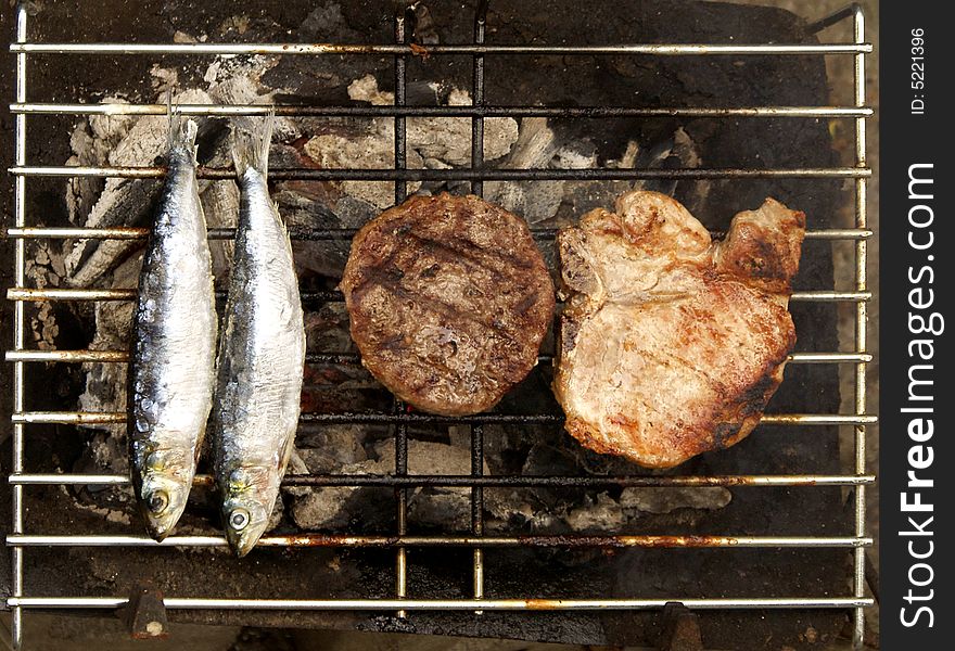 2 mackerel, a beef patty and a porkchop on an outdoor charcoal grill. 2 mackerel, a beef patty and a porkchop on an outdoor charcoal grill