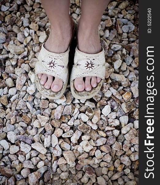 View of womans feet wearing sandals on pile of rocks