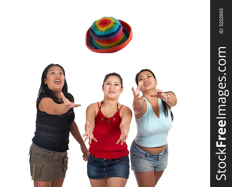 Three playful young women trying to catch the colorful hat