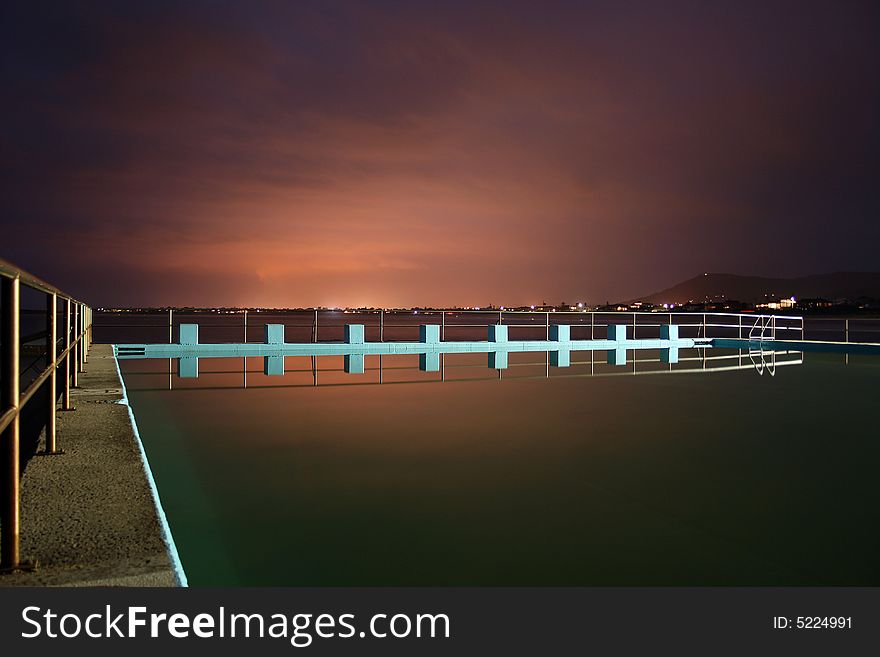 A swimming pool on a still evening, the overcast sky is lit up by southern steel producing factories creating a surreal effect. A swimming pool on a still evening, the overcast sky is lit up by southern steel producing factories creating a surreal effect