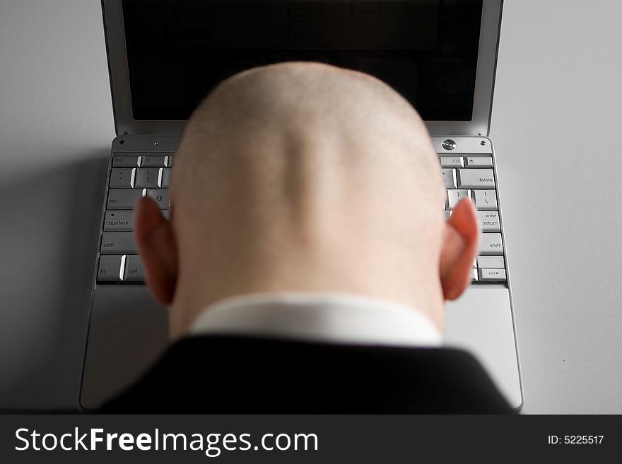 A stressed bald businessman with his forehead resting on the laptop computer keyboard. A stressed bald businessman with his forehead resting on the laptop computer keyboard.