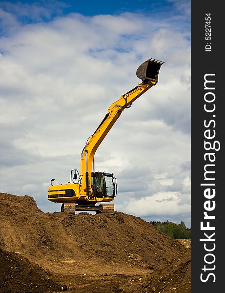 Heavy orange excavator reaches the sky with its powerful arm. It stands on the soil, the background is the dramatic cloudy sky