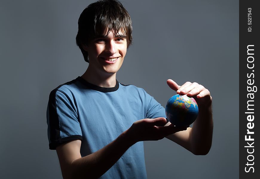 A portrait about a trendy attractive young man who is smiling, he is holding a globe in his hands and he is planning his trip. He is wearing a blue t-shirt. A portrait about a trendy attractive young man who is smiling, he is holding a globe in his hands and he is planning his trip. He is wearing a blue t-shirt.