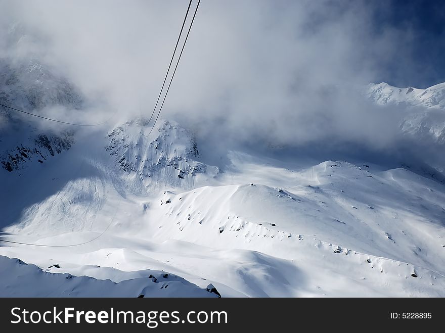 Steel ropes of elevator against snow glacier slope, white clouds and peaks of the Alps, Mont Blanc, France. Steel ropes of elevator against snow glacier slope, white clouds and peaks of the Alps, Mont Blanc, France