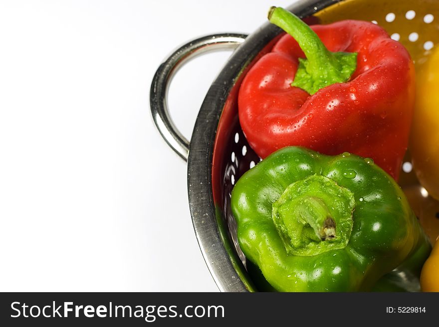 Red and Green Paprikas in Colander on white background