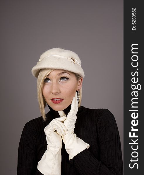 A blonde in a black fur hat and a black turtleneck with her hand on her chin looking up. A blonde in a black fur hat and a black turtleneck with her hand on her chin looking up