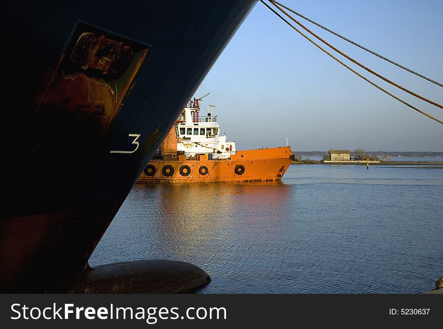 A tugboat / supply vessel slowly manouvres backwards to its bearth. A larger oceangoing vessel is bearthed at the opposite key. A tugboat / supply vessel slowly manouvres backwards to its bearth. A larger oceangoing vessel is bearthed at the opposite key.