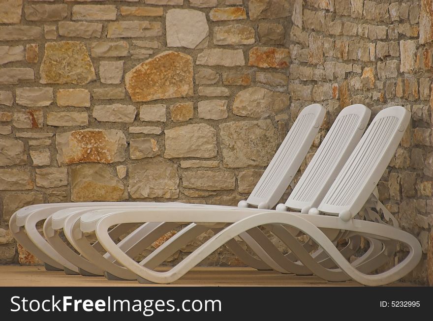 White plastic seats standing on a terrace next to a pool