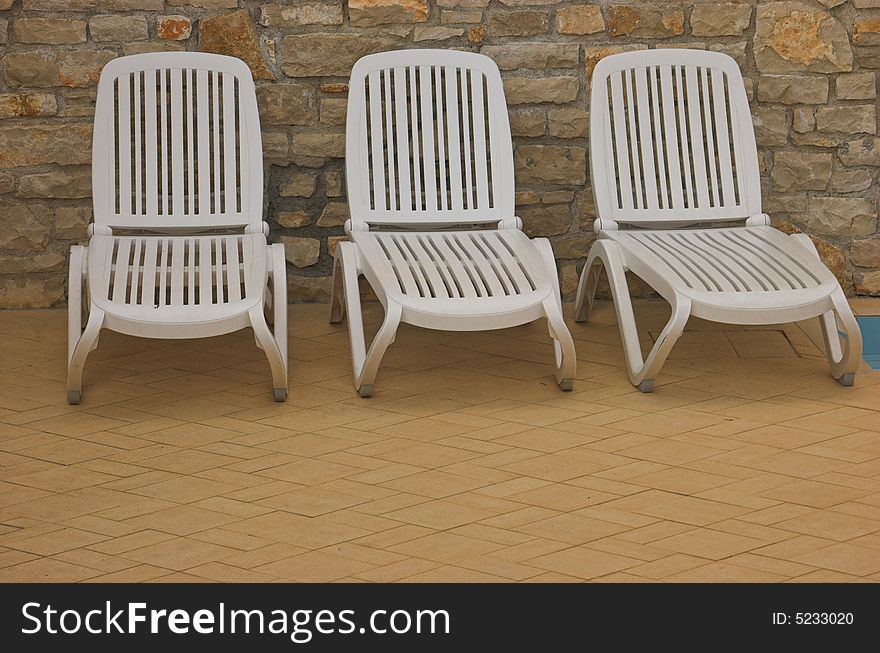 White plastic seats standing on a terrace next to a pool