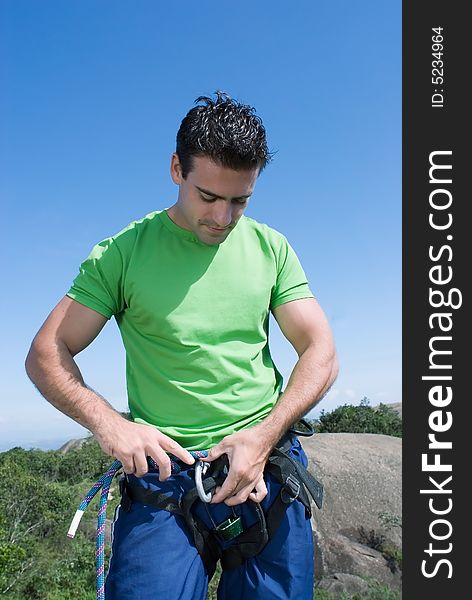 Athletic young climber checking his gear and climbing harness. Vertical shot set against a blue sky. Athletic young climber checking his gear and climbing harness. Vertical shot set against a blue sky.