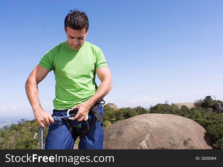 Athletic young climber checking his gear and climbing harness. Horizontal shot set against a blue sky. Athletic young climber checking his gear and climbing harness. Horizontal shot set against a blue sky.