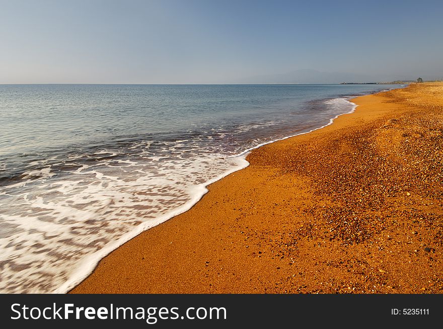 Image shows a long and inviting empty mediterranean beach with bright golden sand. Image shows a long and inviting empty mediterranean beach with bright golden sand.