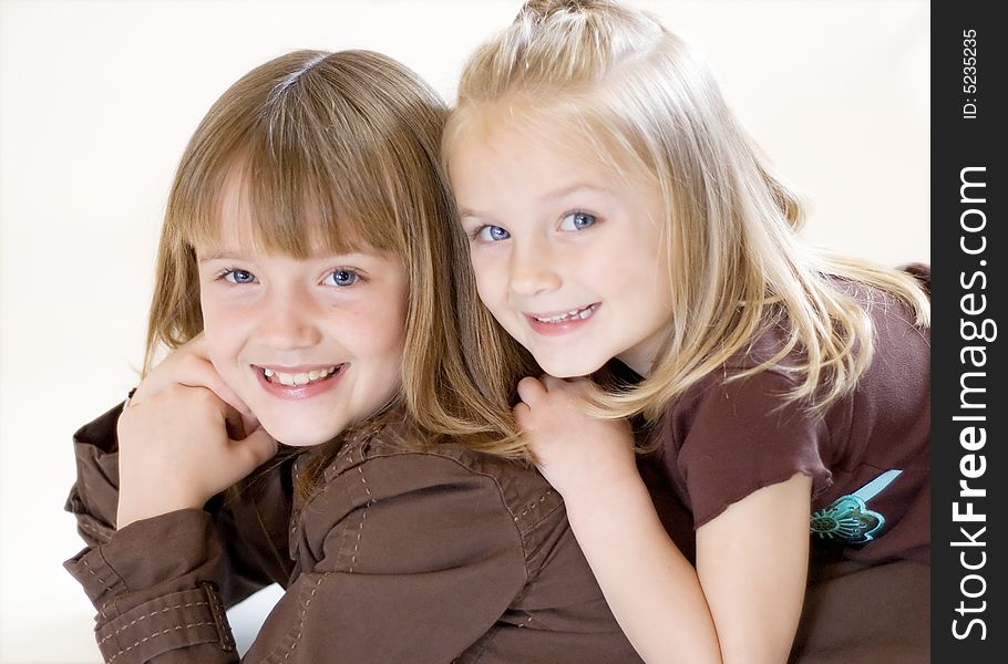 Two cute young sisters posing together in a studio. Horizontally framed shot isolated against a white studio background. Two cute young sisters posing together in a studio. Horizontally framed shot isolated against a white studio background.