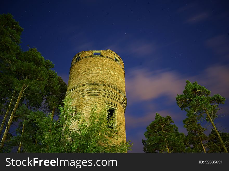 Old water tower made of bricks, surrounded with pines, outskirts of the city at night. Old water tower made of bricks, surrounded with pines, outskirts of the city at night
