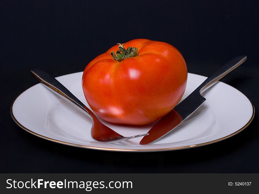 Tomato on the plate vith fork and knife