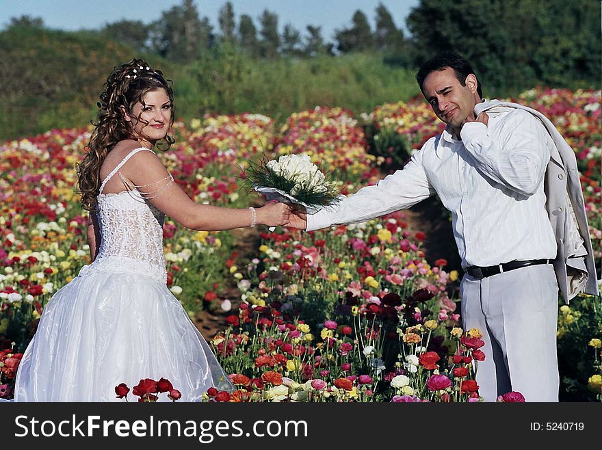 Groom and bride in the flower field holding wreath