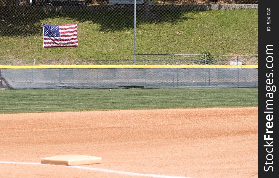 An outfield of a baseball or softball field with an American flag on the fence. An outfield of a baseball or softball field with an American flag on the fence