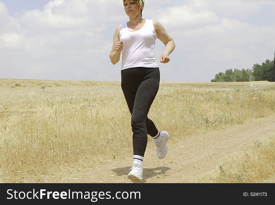 The young woman runs on a path around of a field