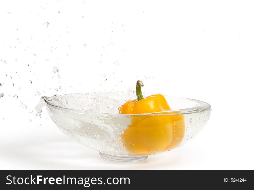 Yellow paprika falling into glass vase with water, splashes. Isolated over white