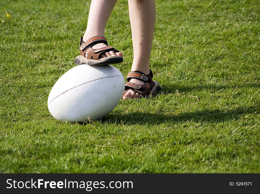 A young boy wearing sandals with a rugby ball on a grass field. A young boy wearing sandals with a rugby ball on a grass field.