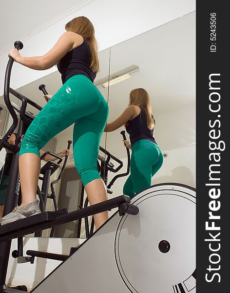 Vertical shot, from below and behind, of a woman using an elliptical machine. Vertical shot, from below and behind, of a woman using an elliptical machine.