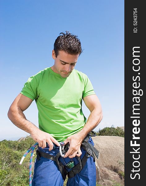 Athletic young man attaching a climbing rope to his climbing harness. Vertically framed shot against a clear blue sky. Vertically framed shot. Athletic young man attaching a climbing rope to his climbing harness. Vertically framed shot against a clear blue sky. Vertically framed shot