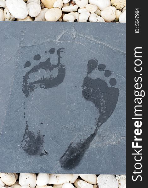 Footprints on a stone tile surrounded by white pebbles.